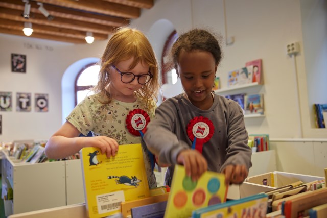 Tv&aring; barn som bl&auml;ddrar i bokl&aring;dor p&aring; ett bibliotek.
